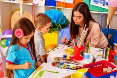 Children with teacher woman painting on paper at table  in  kindergarten . Group people.