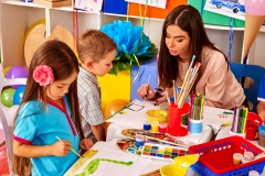 Children with teacher woman painting on paper at table  in  kindergarten . Group people.